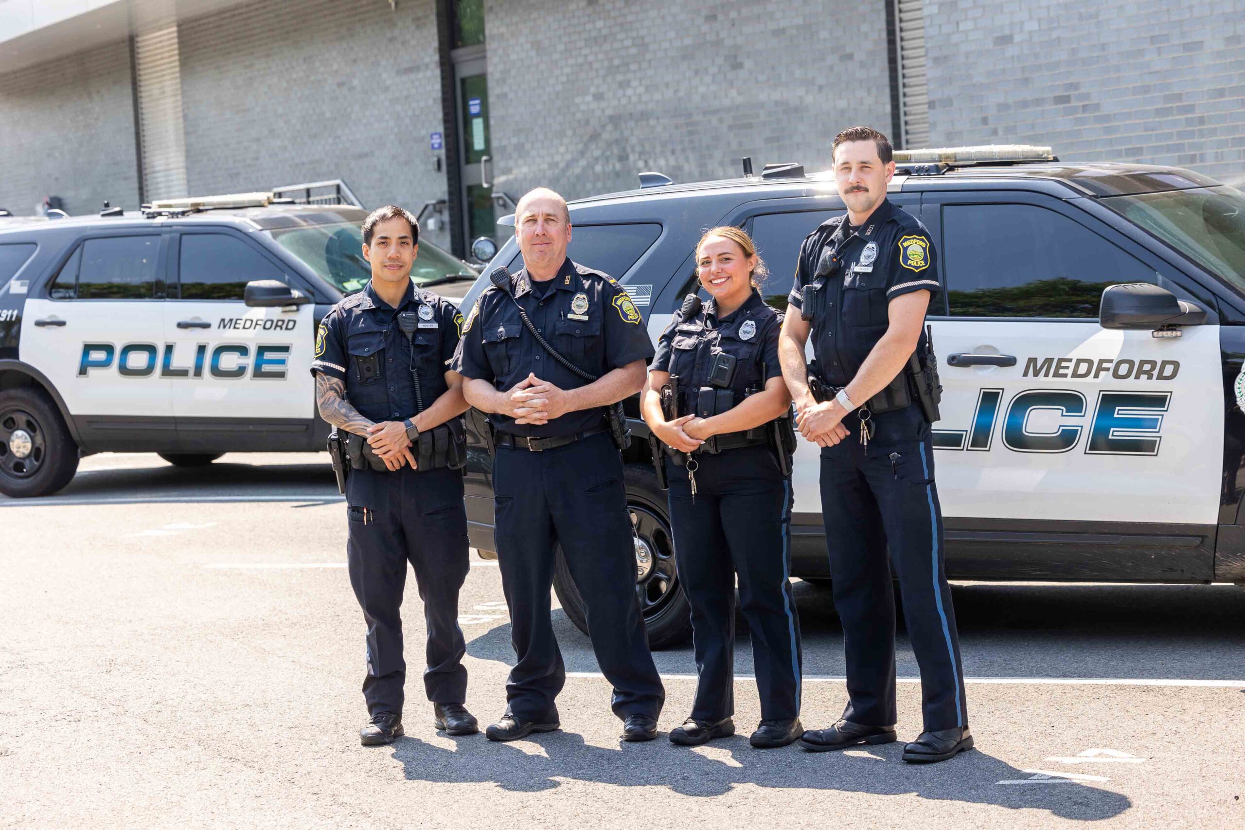 A group of four Medford Police officers standing in front of two cop cars.